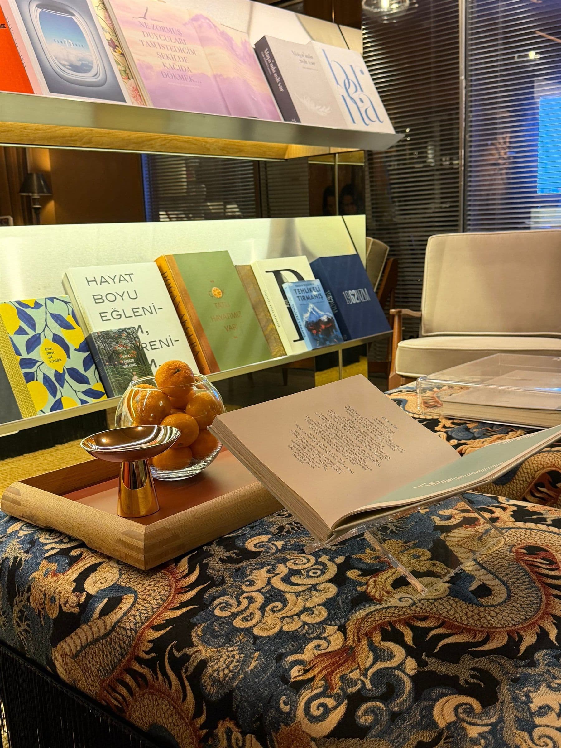 Desenli pufun üzerinde açık bir kitap ve meyve kâsesi